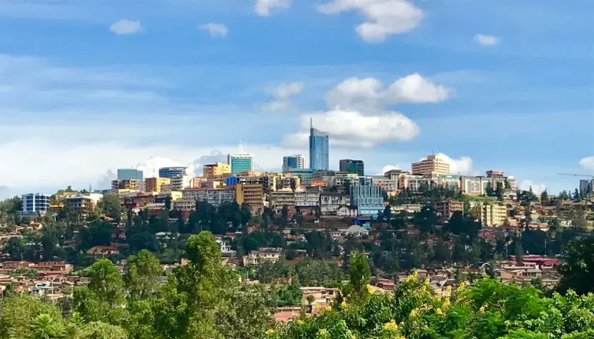 Blick auf die Skyline von Ruanda, Kigali, mit vielen Gebäuden auf grünen Hügeln unter einem blauen Himmel mit Wolken.