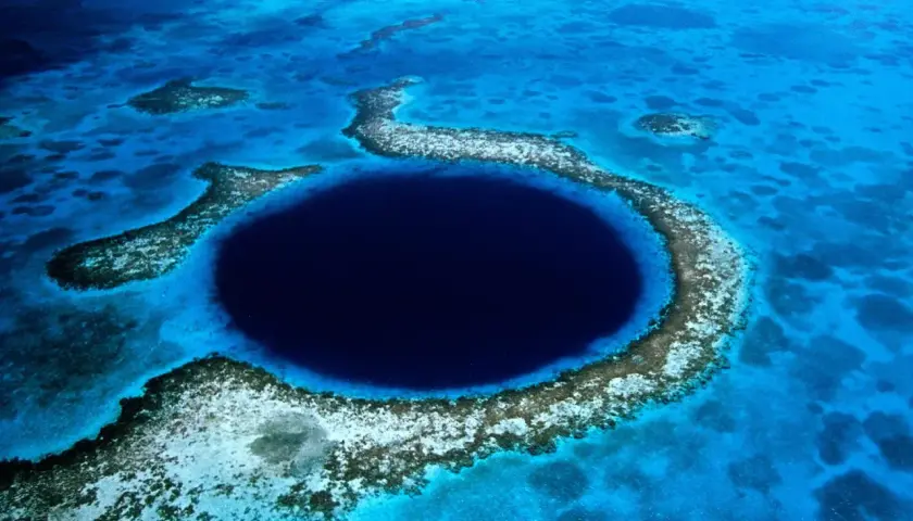 Das Belize Blue Hole, ein tiefes, kreisförmiges Loch im Meer, umgeben von Korallenriffen und türkisfarbenem Wasser.