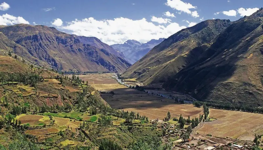 Weites Tal in den Peru Anden, mit terrassierten Feldern, einem Fluss und einem Dorf.