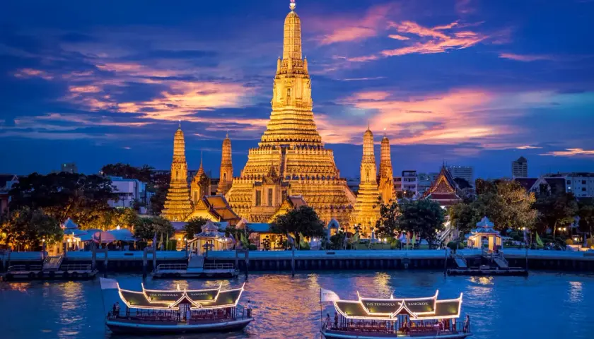 Wat Arun im Abendlicht, ein absolutes Bangkok Must-See. Boote auf dem Fluss vor dem beleuchteten Tempel.