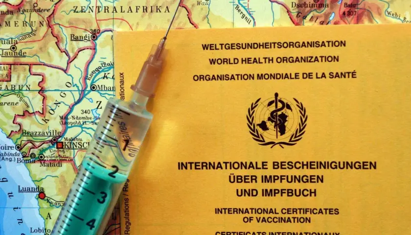 Gelber Impfpass der WHO liegt auf einer Karte von Zentralafrika. Spritze daneben. Wichtig für Reisen nach Malaysia, Impfungen sind oft Pflicht.