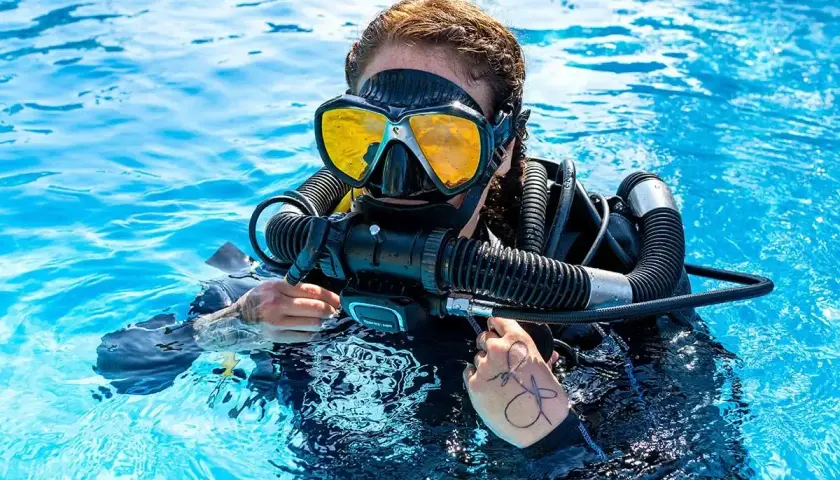 Taucherin mit gelber Maske und Atemregler im klaren Wasser, bereit für das Tauchen auf Bali.