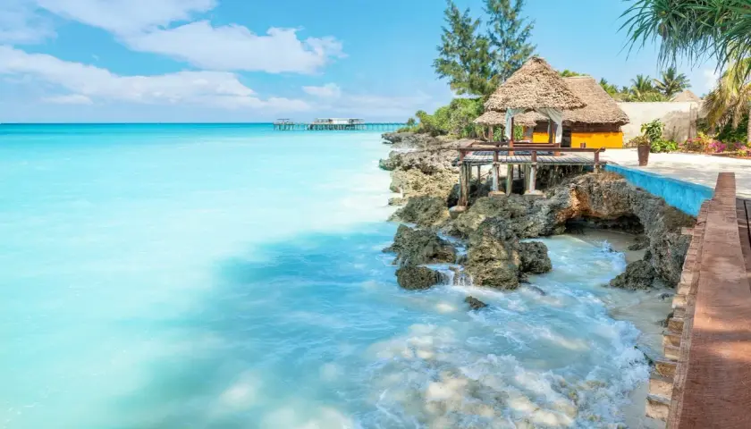 Traumhaftes Sansibar Wetter im Mai: Türkises Meer trifft auf felsige Küste mit Strohdach-Bungalows. Perfekt für einen entspannten Urlaub.