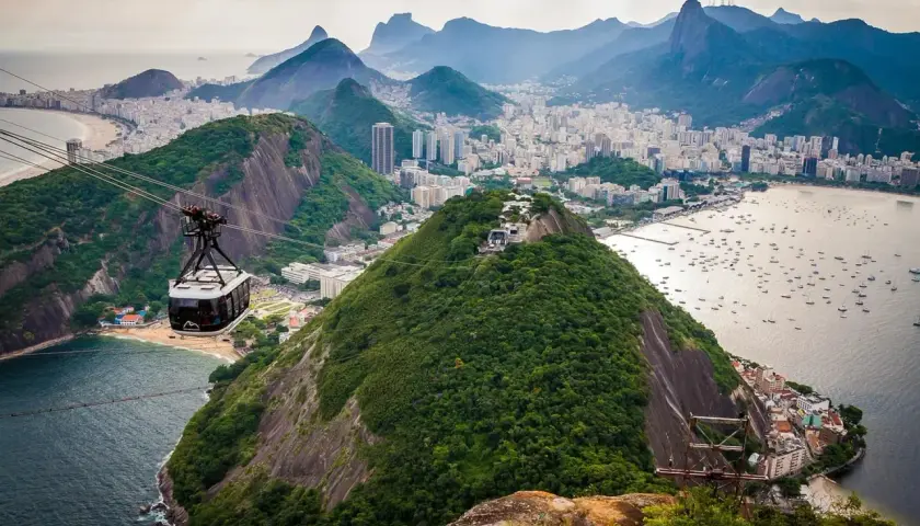 Seilbahnfahrt zum Zuckerhut in Rio de Janeiro. Die Stadt erstreckt sich unterhalb, Boote liegen im Wasser.