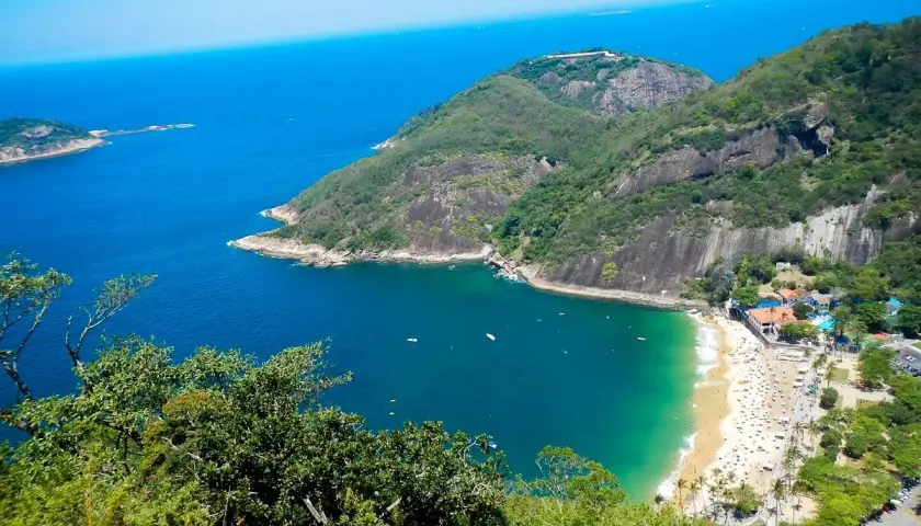 Blick vom Morro da Urca auf eine Bucht mit Strand, Palmen und dem tiefblauen Meer.