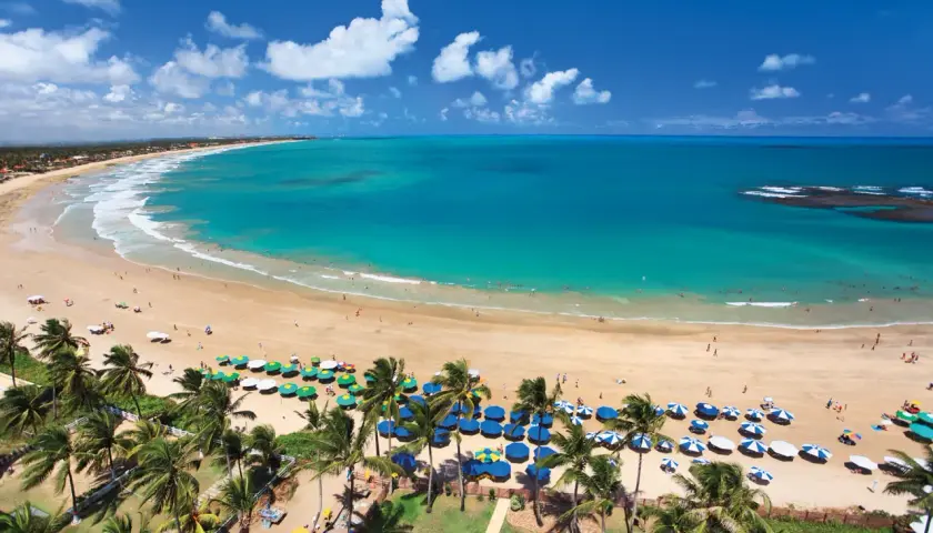 Traumhafter Strand von Porto de Galinhas mit türkisfarbenem Wasser, Palmen und vielen bunten Sonnenschirmen.