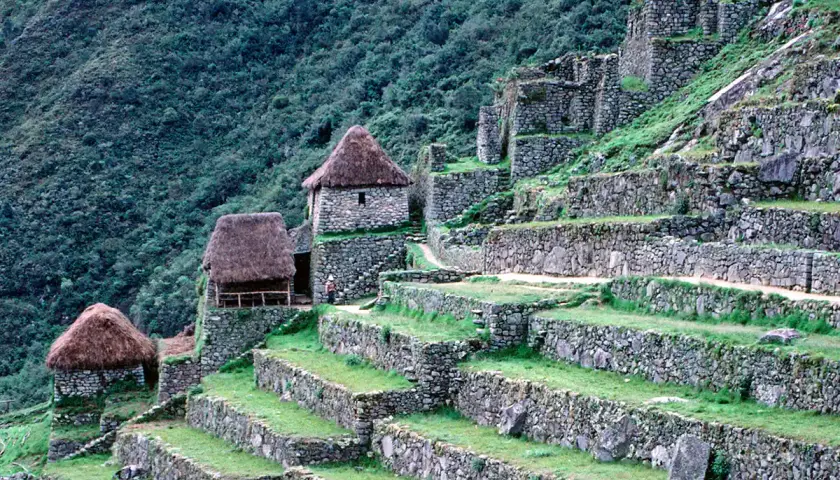 Terrassen und Steinhäuser der Machu Picchu Rekonstruktion, eingebettet in einen grünen Berghang.