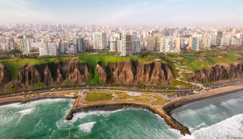 Blick auf die Küste von Lima, wo grüne Hügel auf das Meer treffen. Hochhäuser säumen die Stadt, während die lima einwohner die Küstenpromenade genießen.