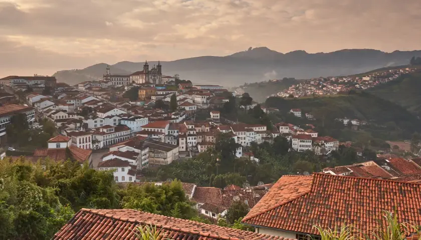 Malerische Hügelstadt Ouro Preto im Morgendunst, mit traditionellen Häusern und einer Kirche im Hintergrund.