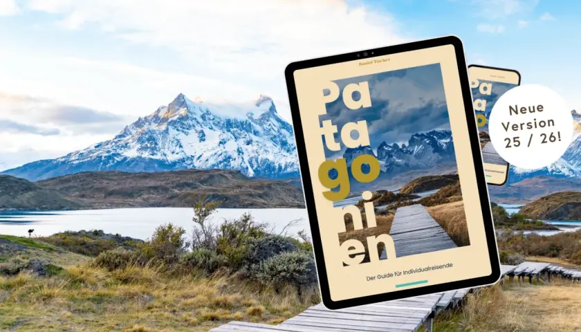 Ein Tablet mit dem Titel "Patagonien" liegt vor einer atemberaubenden Berglandschaft. Der Reiseführer ist die neue Version 25/26.