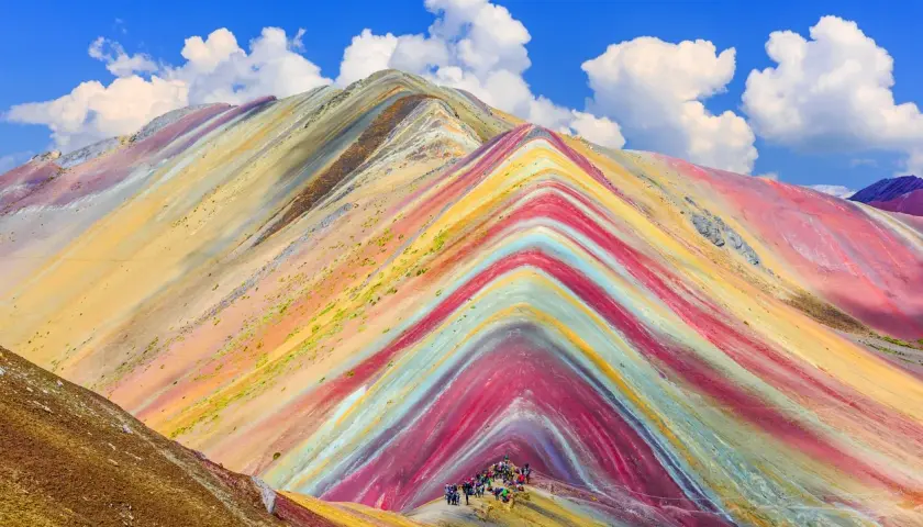 Bunte Streifen ziehen sich über die Berge, wie ein natürlicher Regenbogen. Eine Gruppe Wanderer erkundet diese farbenprächtige Landschaft.