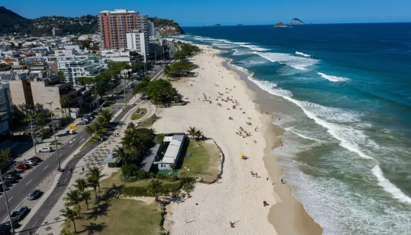 Blick auf den Strand von Barra da Tijuca mit Wellen, Palmen und Gebäuden.