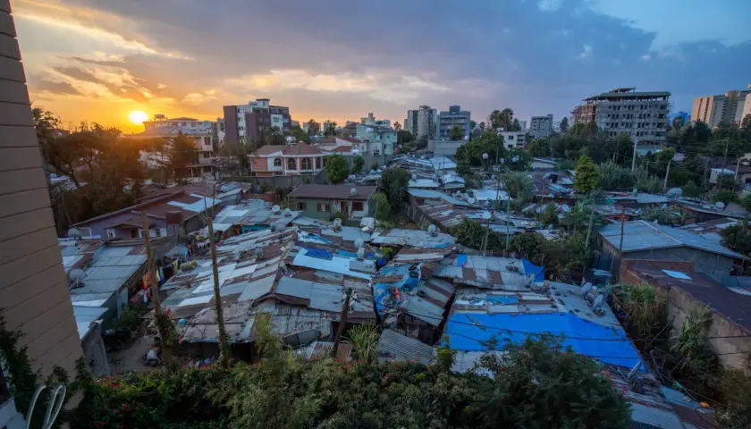 Sonnenuntergang über Addis Abeba. Dächer aus Wellblech und Planen prägen das Bild, während im Hintergrund moderne Gebäude emporragen. Die **Addis Abeba Sicherheit** ist ein komplexes Thema, das sich in diesem Kontrast widerspiegelt.