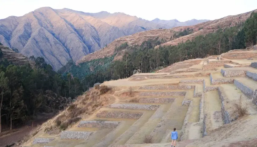 Terrassenanlagen im heiligen Tal Peru, mit einer Person, die die antiken Stätten erkundet, vor einer majestätischen Bergkulisse.