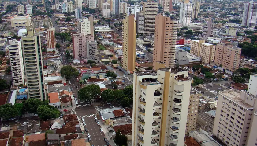 Blick über eine Stadt mit vielen Hochhäusern und kleineren Gebäuden. Ein langer, heller Turm dominiert das Bild, umgeben von weiteren Wohn- und Bürogebäuden. Ein typisches Bild von Campo Grande.