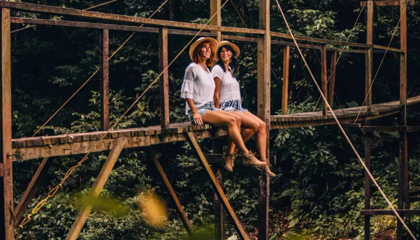Zwei Frauen mit Hüten sitzen auf einer Holzbrücke im peruanischen Amazonas.