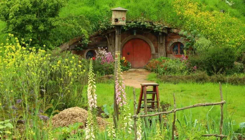 Ein Hobbit-Dorf in Neuseeland, mit einem runden roten Tor, umgeben von üppiger Natur und bunten Blumen.
