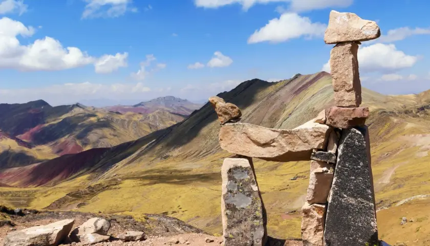 Bunte Berge in Peru, bekannt als Regenbogenberg, mit einer Steinpyramide im Vordergrund.