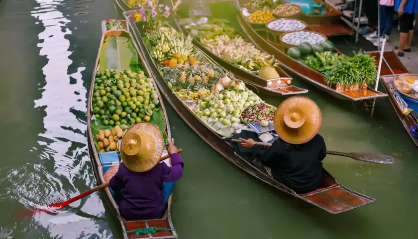 Bunte Boote voller Früchte und Gemüse auf einem **floating market**. Händler mit traditionellen Hüten rudern durch das Wasser.