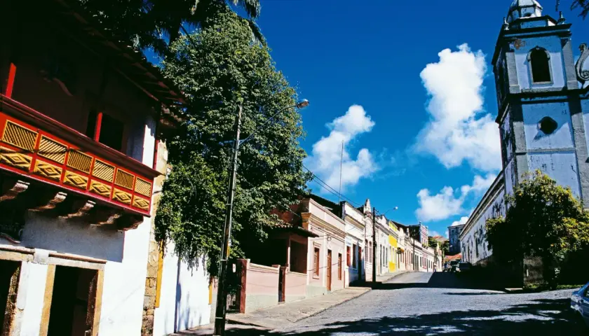 Bunte Kolonialhäuser und Kirche säumen eine Kopfsteinpflasterstraße unter blauem Himmel.