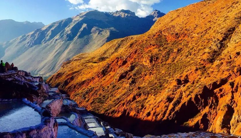 Terrassierte Salinen von Maras, Peru, im warmen Licht der untergehenden Sonne. Die Berge im Hintergrund sind in Schatten getaucht.