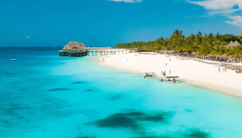 Traumhafter Strand auf Sansibar mit türkisfarbenem Wasser, Palmen und einem Steg.