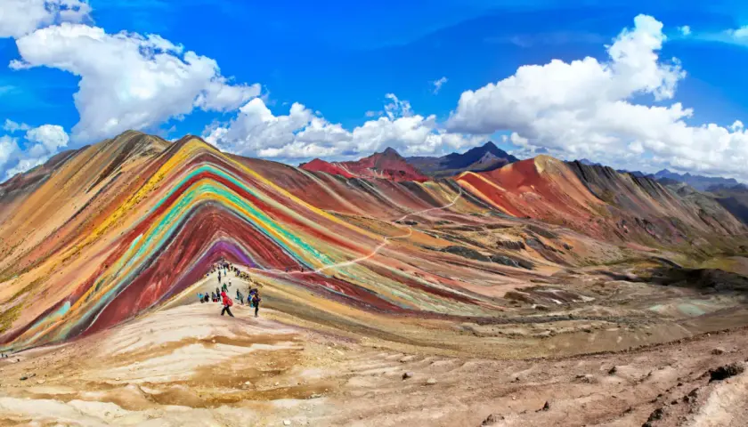 Regenbogenberg in Peru im September. Wanderer bestaunen die bunten Mineralstreifen der Berge unter blauem Himmel.