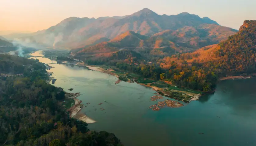 Sonnenuntergang über dem Mekong Delta. Berge, Wälder und ein breiter Fluss mit kleinen Booten.