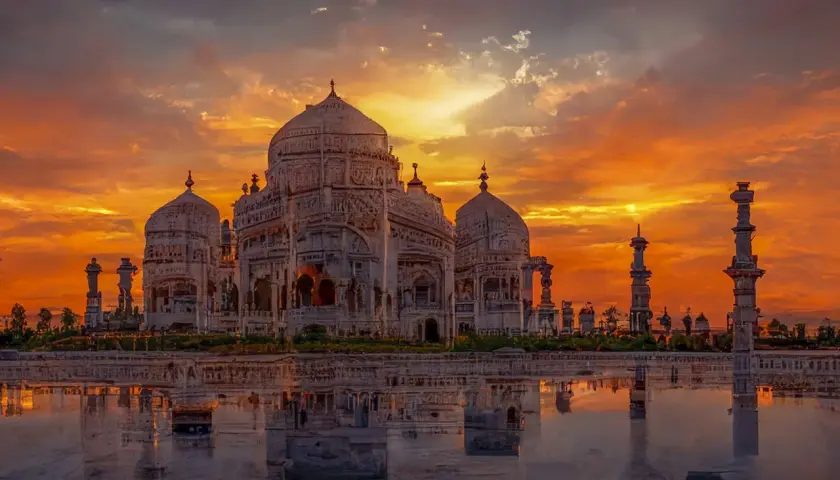 Das Taj Mahal spiegelt sich im Wasser, während ein dramatischer Sonnenuntergang den Himmel in leuchtenden Orange- und Rottönen färbt.