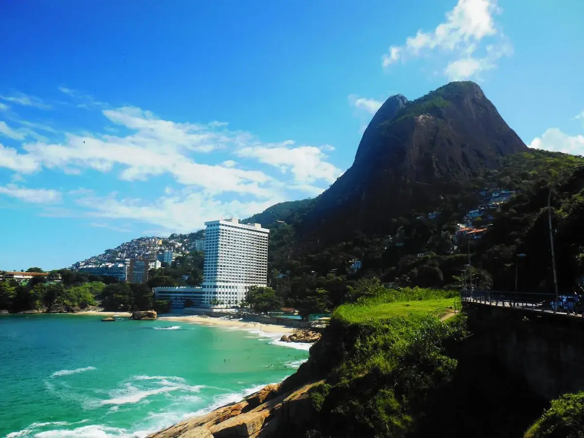 Traumhafter Blick auf Leblon, Rio de Janeiro: Türkisfarbenes Meer, ein Strand mit Palmen und das imposante Sheraton Hotel vor einem Berg.