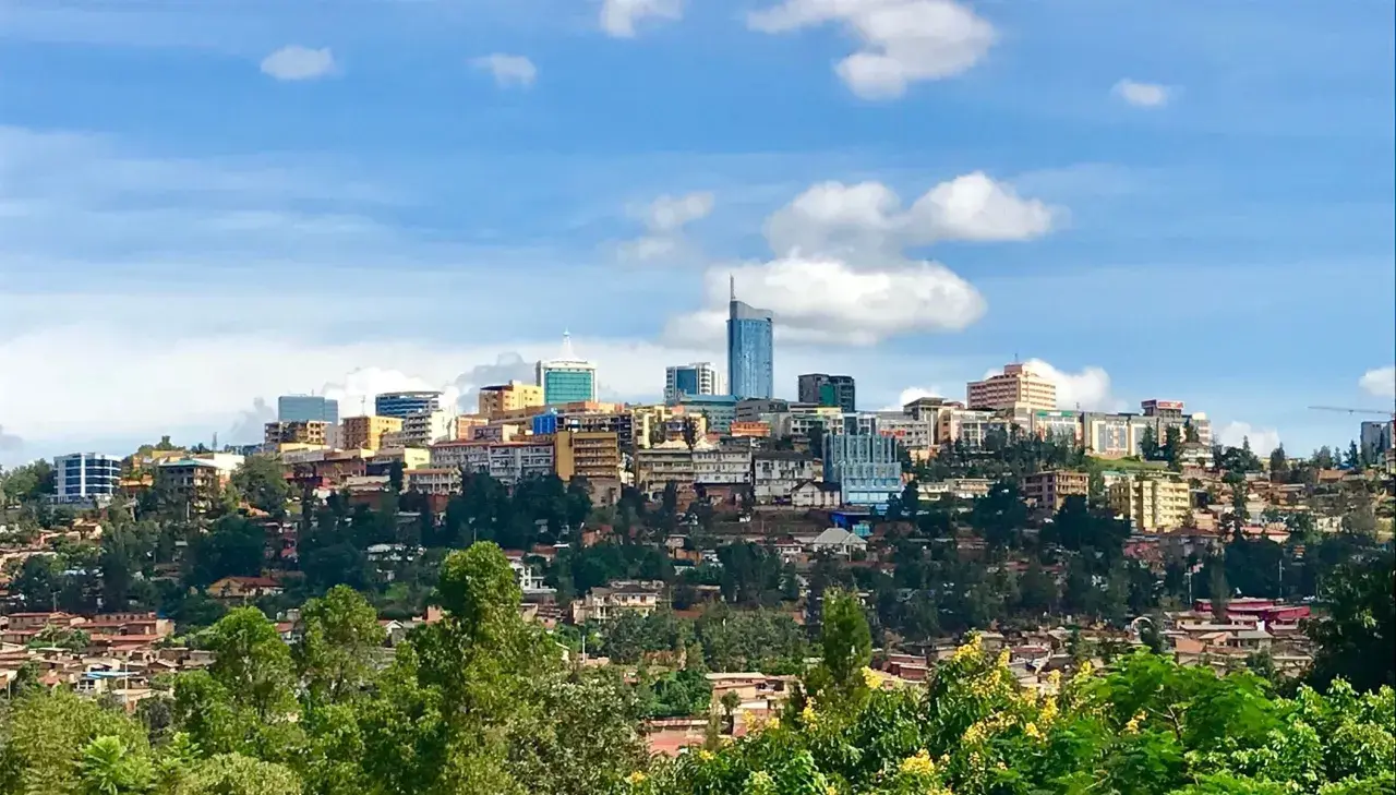 Blick auf die Skyline von Ruanda, Kigali, mit vielen Gebäuden auf grünen Hügeln unter einem blauen Himmel mit Wolken.