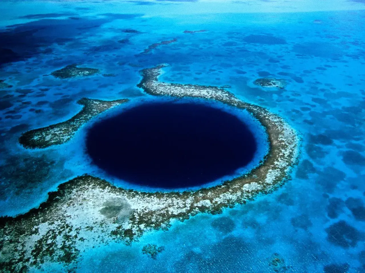 Das Belize Blue Hole, ein tiefes, kreisförmiges Loch im Meer, umgeben von Korallenriffen und türkisfarbenem Wasser.