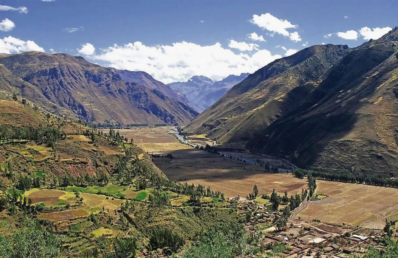 Weites Tal in den Peru Anden, mit terrassierten Feldern, einem Fluss und einem Dorf.