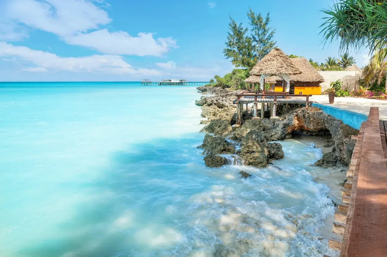 Traumhaftes Sansibar Wetter im Mai: Türkises Meer trifft auf felsige Küste mit Strohdach-Bungalows. Perfekt für einen entspannten Urlaub.
