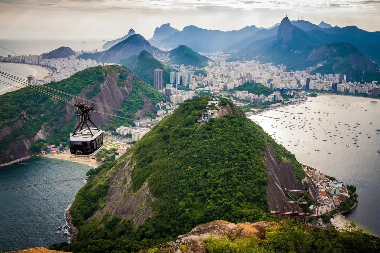 Seilbahnfahrt zum Zuckerhut in Rio de Janeiro. Die Stadt erstreckt sich unterhalb, Boote liegen im Wasser.