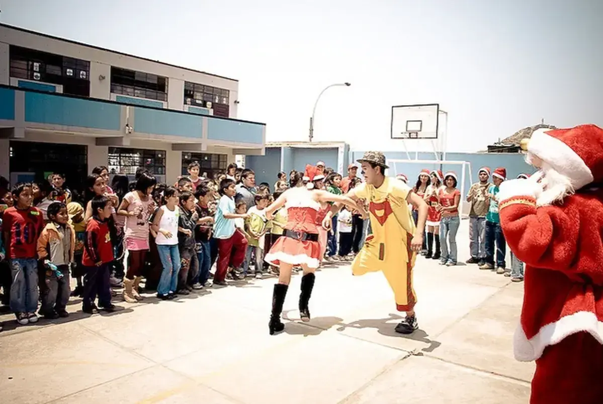 Kinder und Erwachsene feiern Weihnachten in Peru. Ein Nikolaus, eine Weihnachtsfrau und ein Clown unterhalten die Menge.