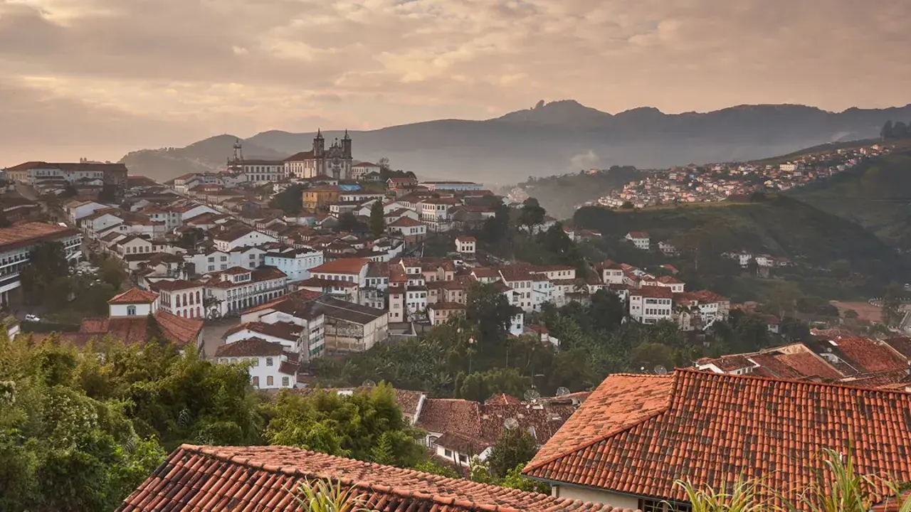 Malerische Hügelstadt Ouro Preto im Morgendunst, mit traditionellen Häusern und einer Kirche im Hintergrund.