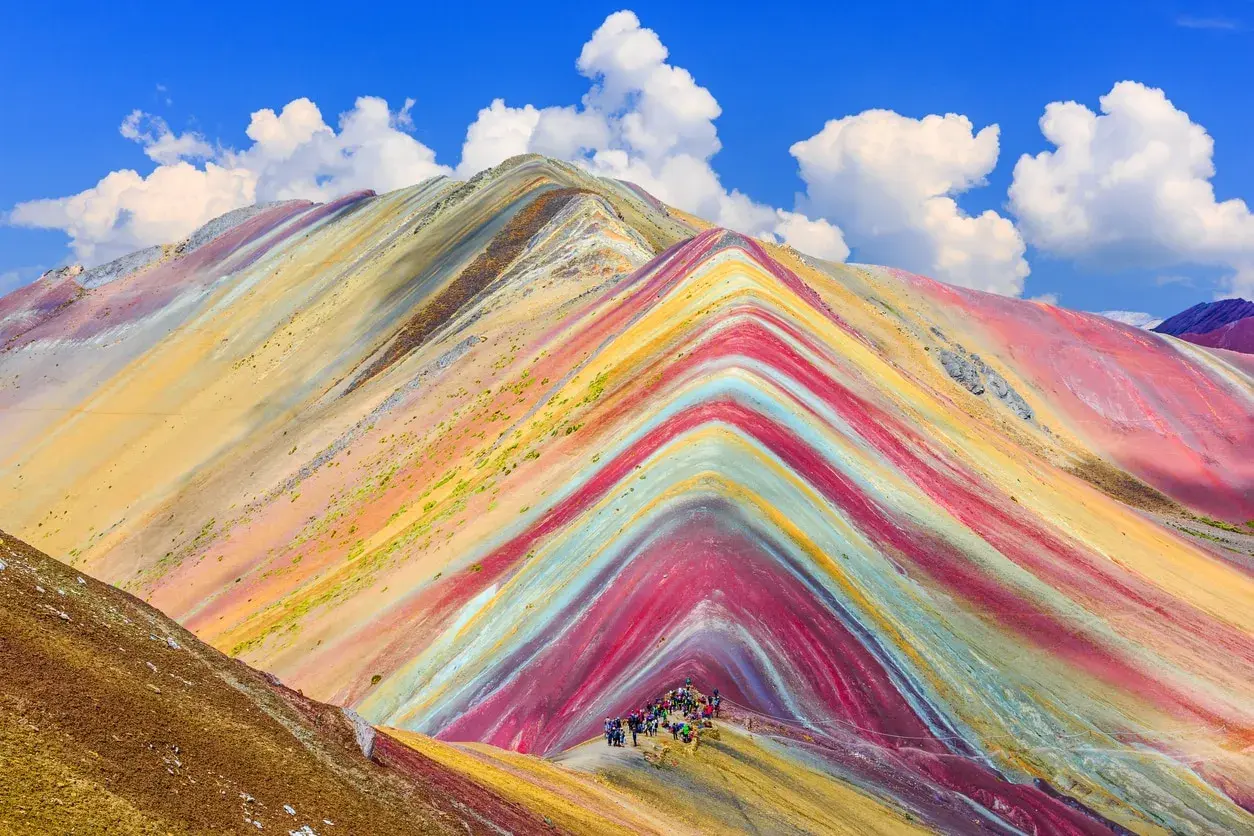 Bunte Streifen ziehen sich über die Berge, wie ein natürlicher Regenbogen. Eine Gruppe Wanderer erkundet diese farbenprächtige Landschaft.