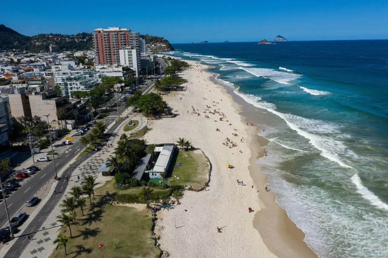 Blick auf den Strand von Barra da Tijuca mit Wellen, Palmen und Gebäuden.