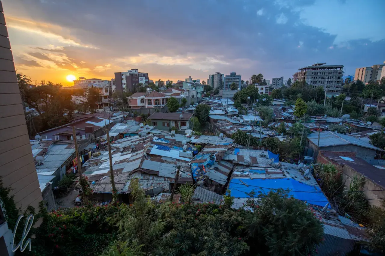 Sonnenuntergang über Addis Abeba. Dächer aus Wellblech und Planen prägen das Bild, während im Hintergrund moderne Gebäude emporragen. Die **Addis Abeba Sicherheit** ist ein komplexes Thema, das sich in diesem Kontrast widerspiegelt.