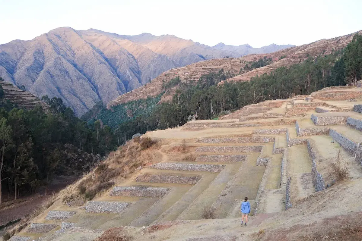 Terrassenanlagen im heiligen Tal Peru, mit einer Person, die die antiken Stätten erkundet, vor einer majestätischen Bergkulisse.