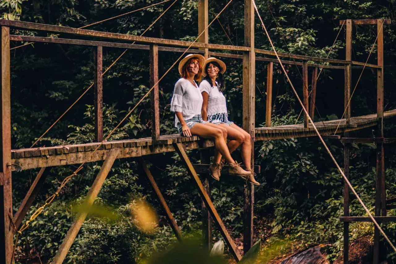 Zwei Frauen mit Hüten sitzen auf einer Holzbrücke im peruanischen Amazonas.