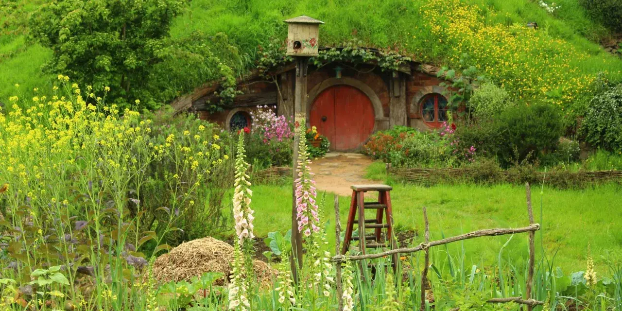 Ein Hobbit-Dorf in Neuseeland, mit einem runden roten Tor, umgeben von üppiger Natur und bunten Blumen.