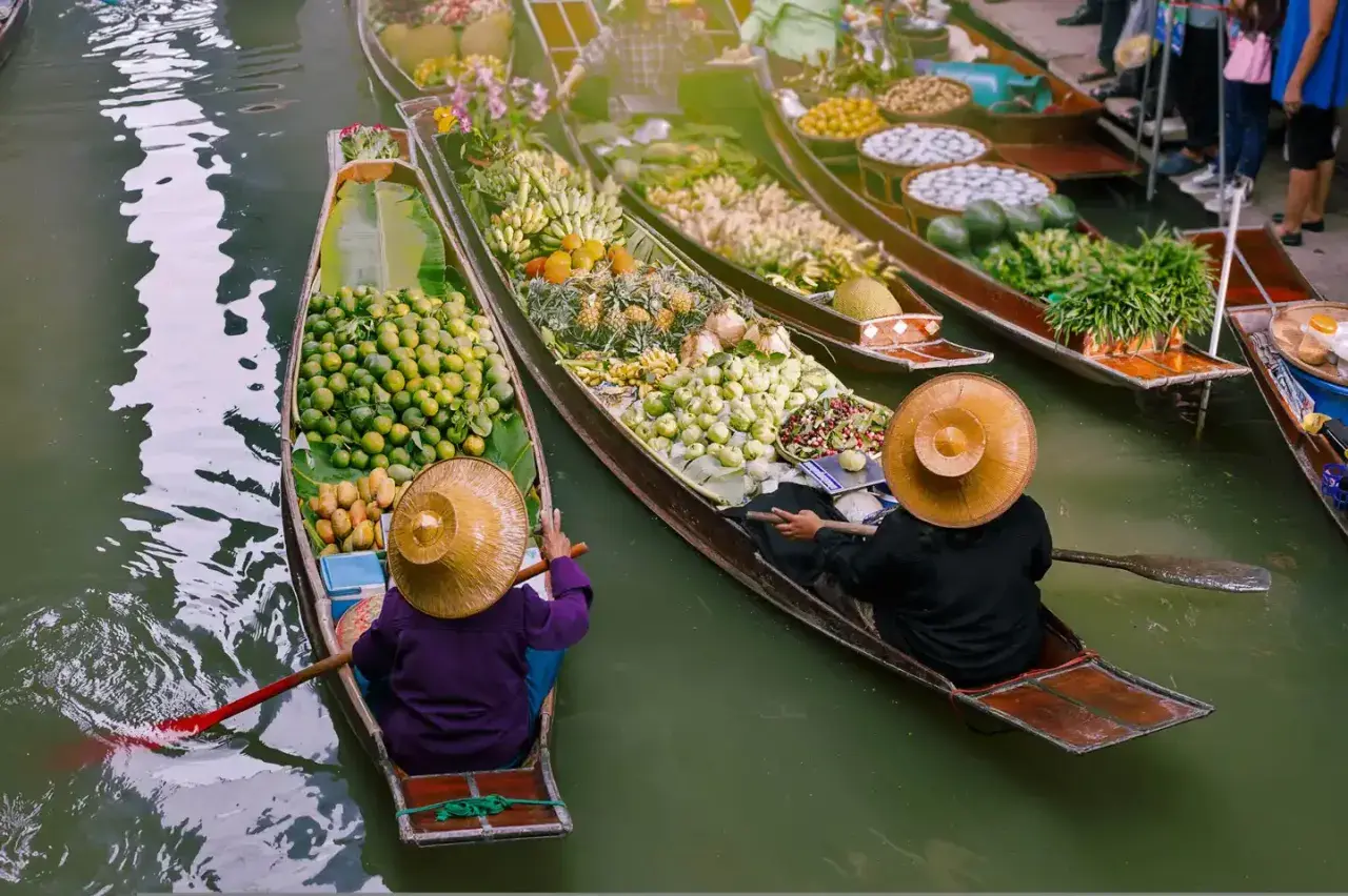 Bunte Boote voller Früchte und Gemüse auf einem **floating market**. Händler mit traditionellen Hüten rudern durch das Wasser.
