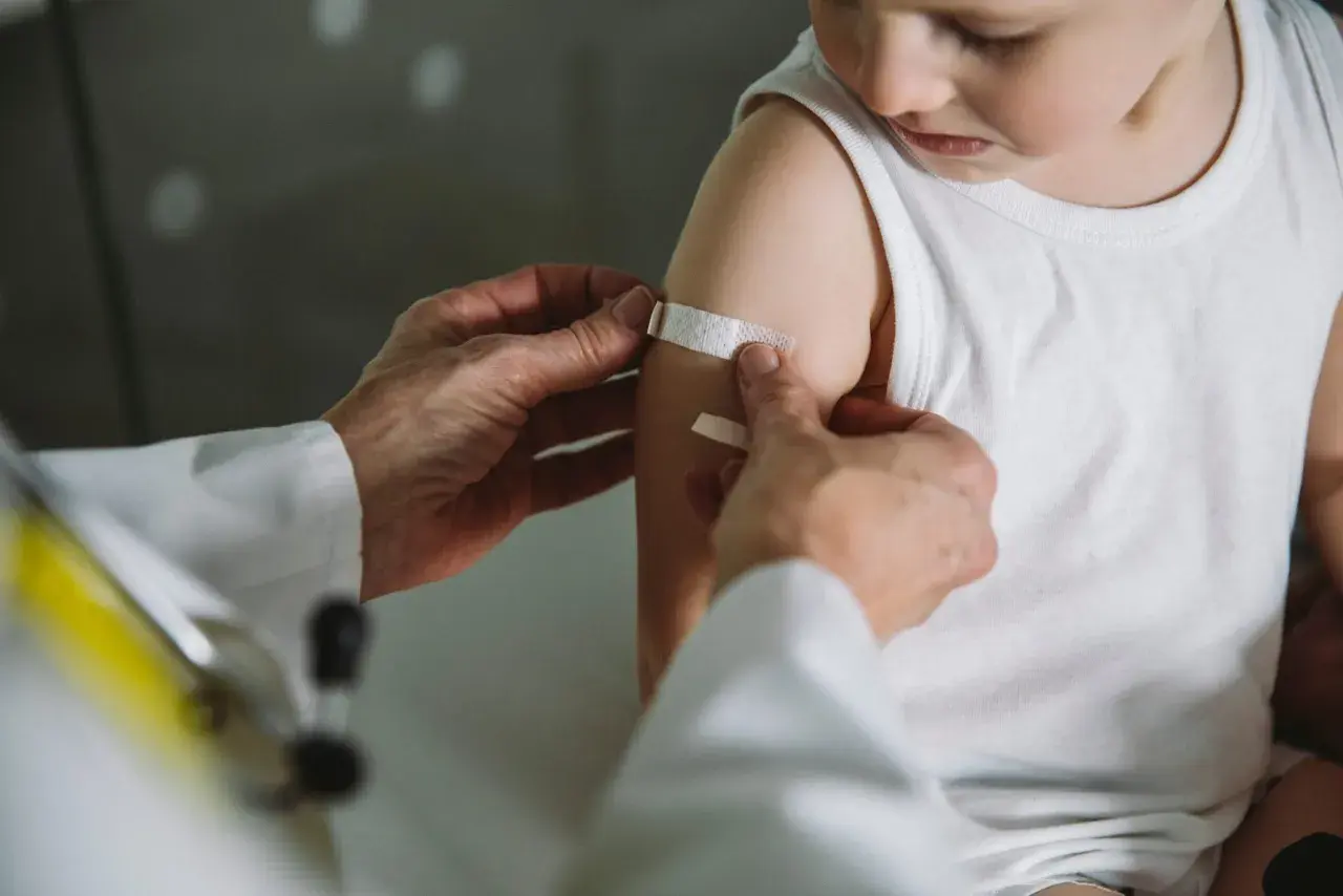 Arzt legt Pflaster auf Arm eines Kindes nach Impfung in Thailand. Kindergesundheit ist wichtig.