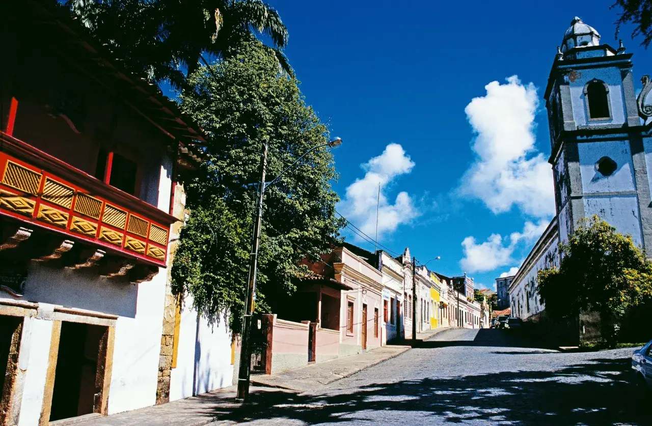 Bunte Kolonialhäuser und Kirche säumen eine Kopfsteinpflasterstraße unter blauem Himmel.