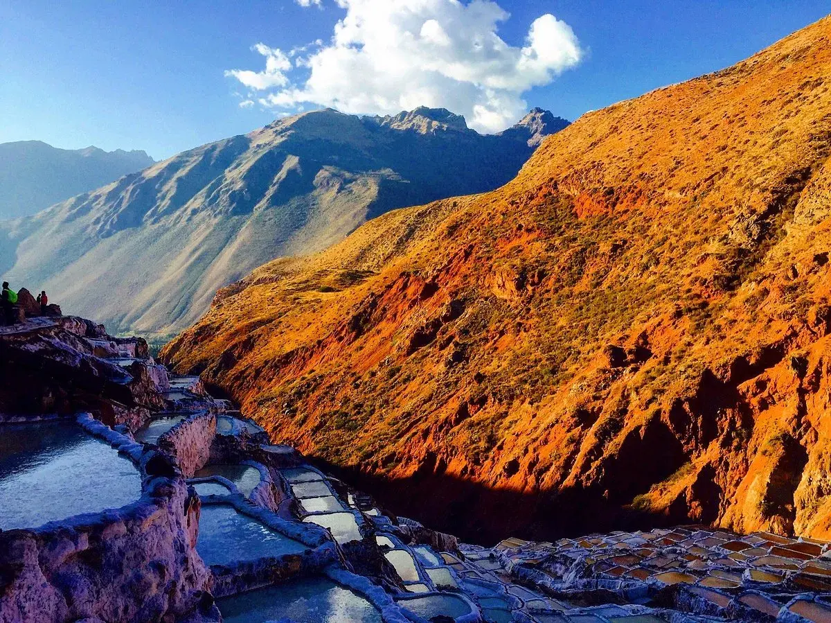 Terrassierte Salinen von Maras, Peru, im warmen Licht der untergehenden Sonne. Die Berge im Hintergrund sind in Schatten getaucht.