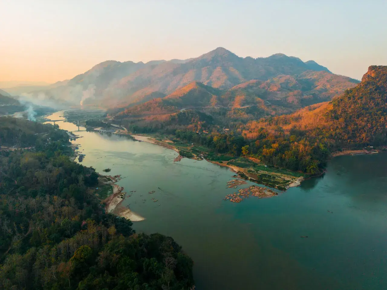 Sonnenuntergang über dem Mekong Delta. Berge, Wälder und ein breiter Fluss mit kleinen Booten.