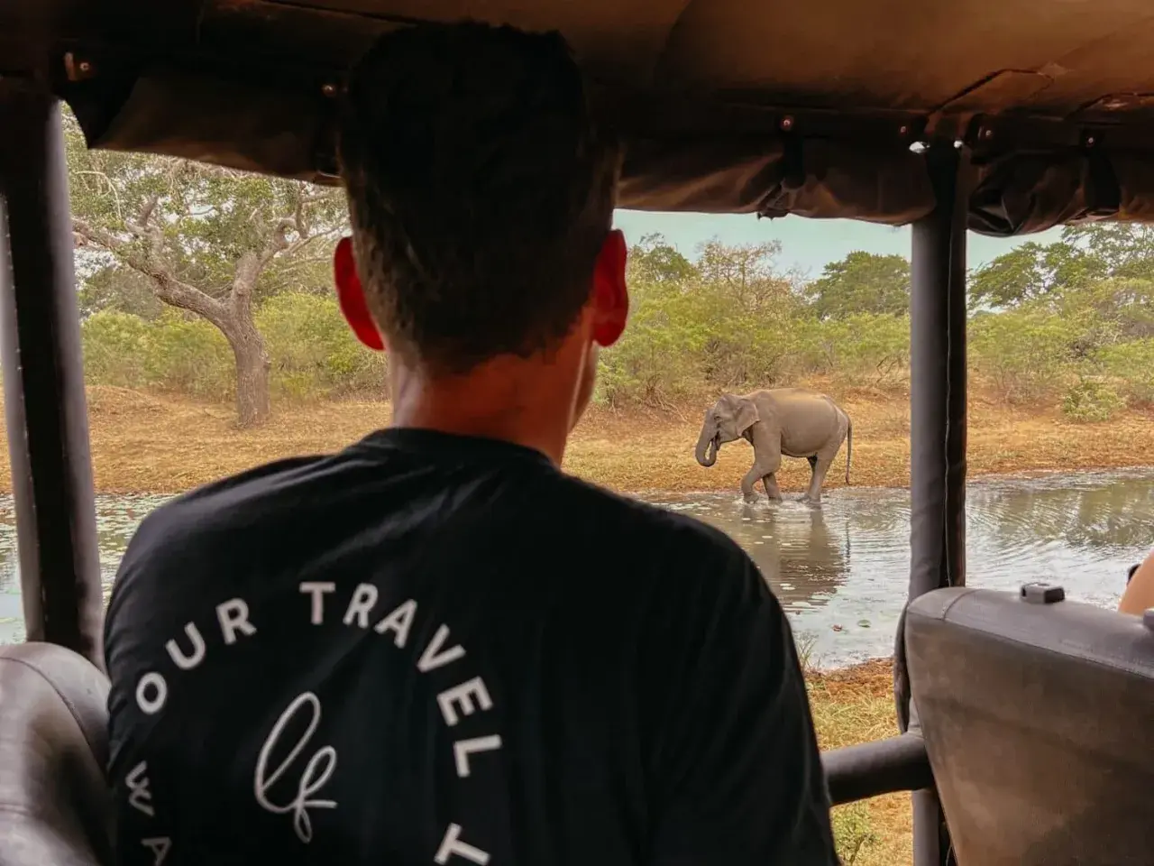 Ein Elefant trinkt im Yala Nationalpark Sri Lanka, während ein Safari-Besucher zusieht.
