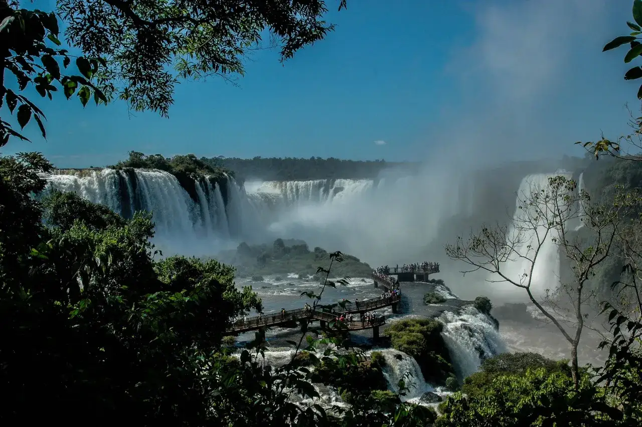 Ein breiter Wasserfall, der in einen Fluss stürzt, umgeben von üppiger Vegetation. Besucher stehen auf Stegen und genießen die Aussicht auf den campo grande.